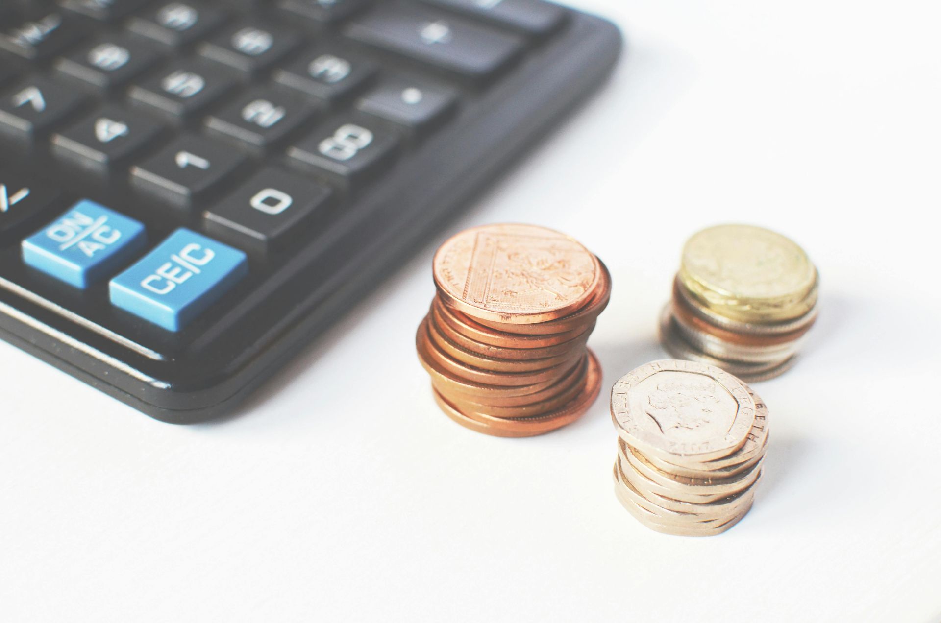 Calculator next to stacks of coins on a white surface, showing budgeting or savings concept
