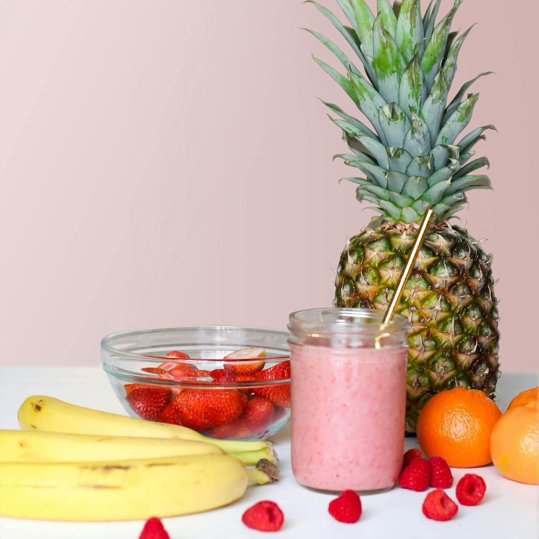 A smoothie in a jar next to a bowl of fruit and a pineapple