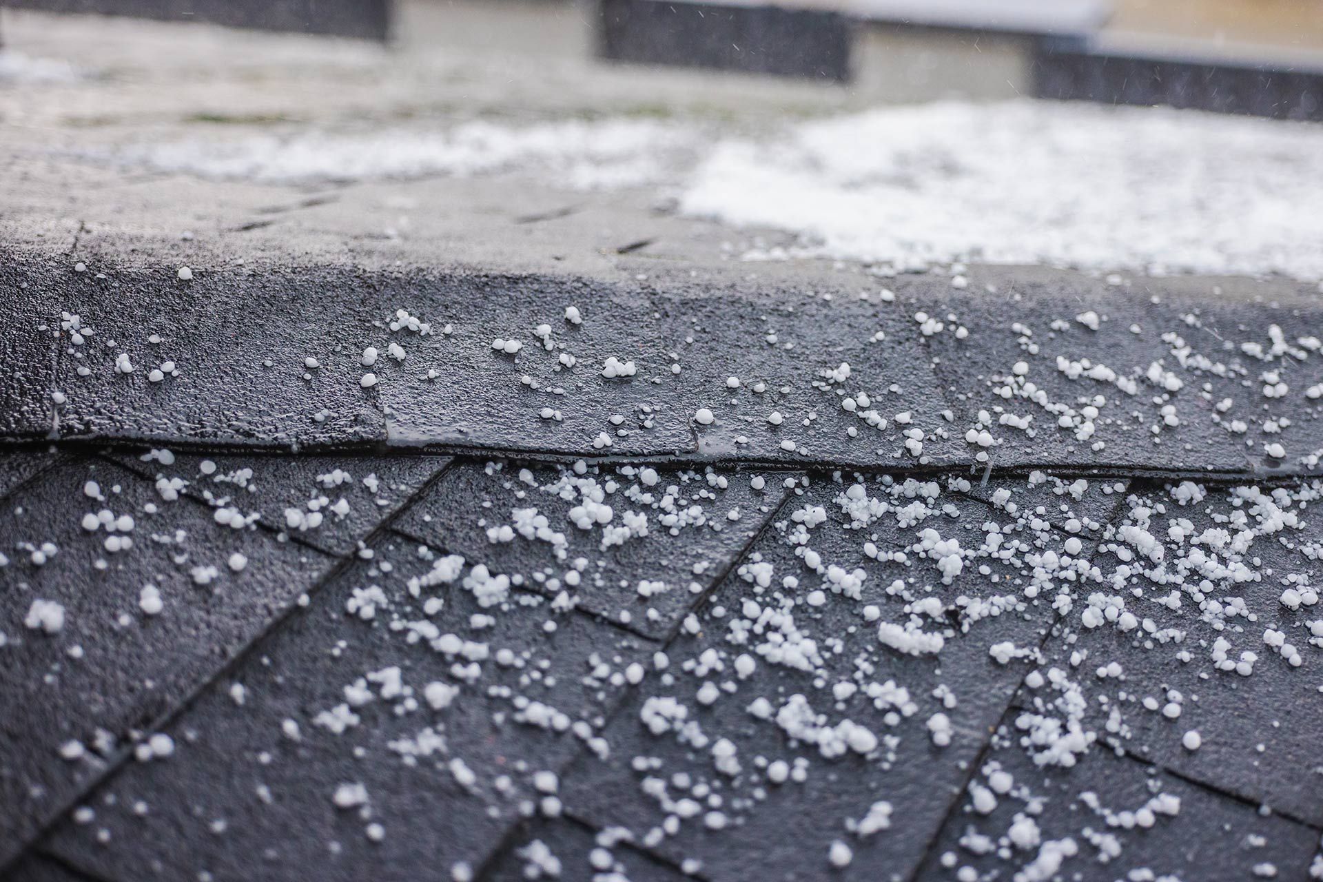 Snow and hail on dark roof shingles and pavement