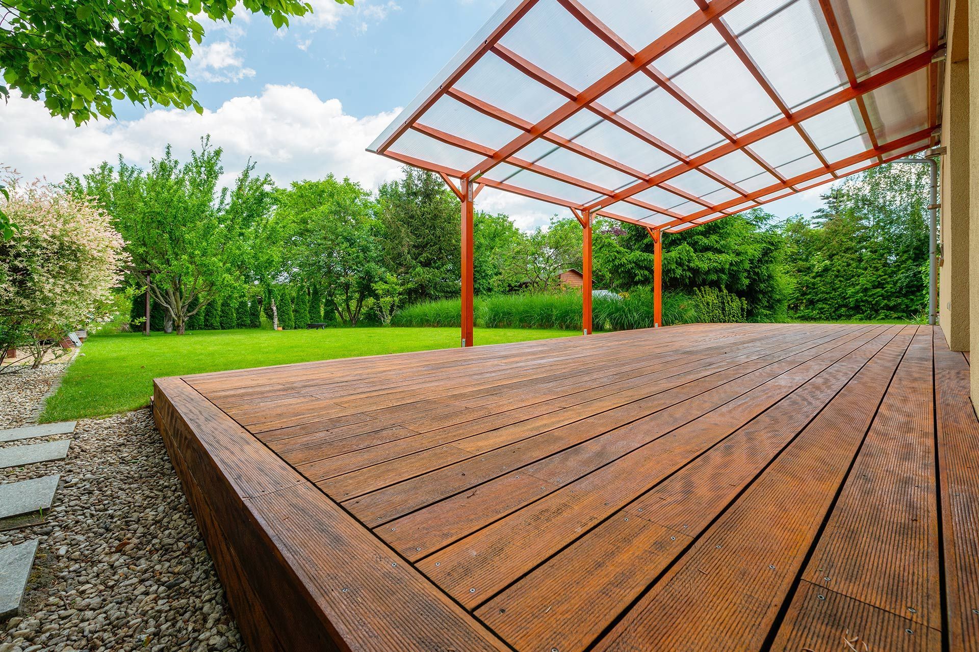 Wooden deck with red pergola roof overlooking a green lawn and trees