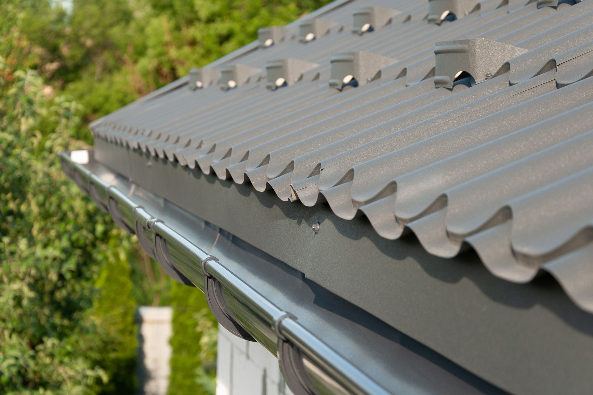 Close-up of a gray corrugated metal roof with vents against a blurred green background