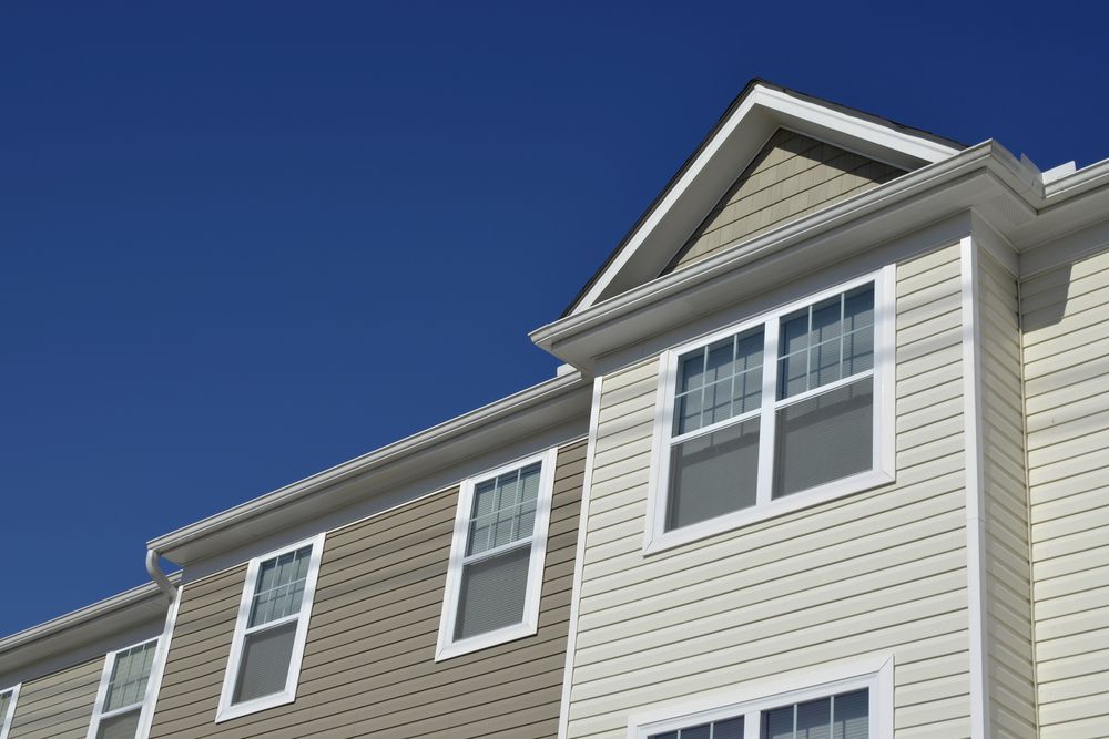 Low-angle view of a beige house with white trim and multiple windows against a clear blue sky