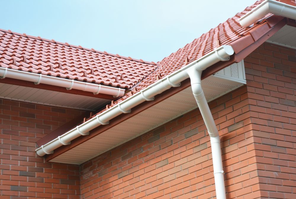 Brick house exterior with red tiled roof, white gutters, and downspout under a blue sky
