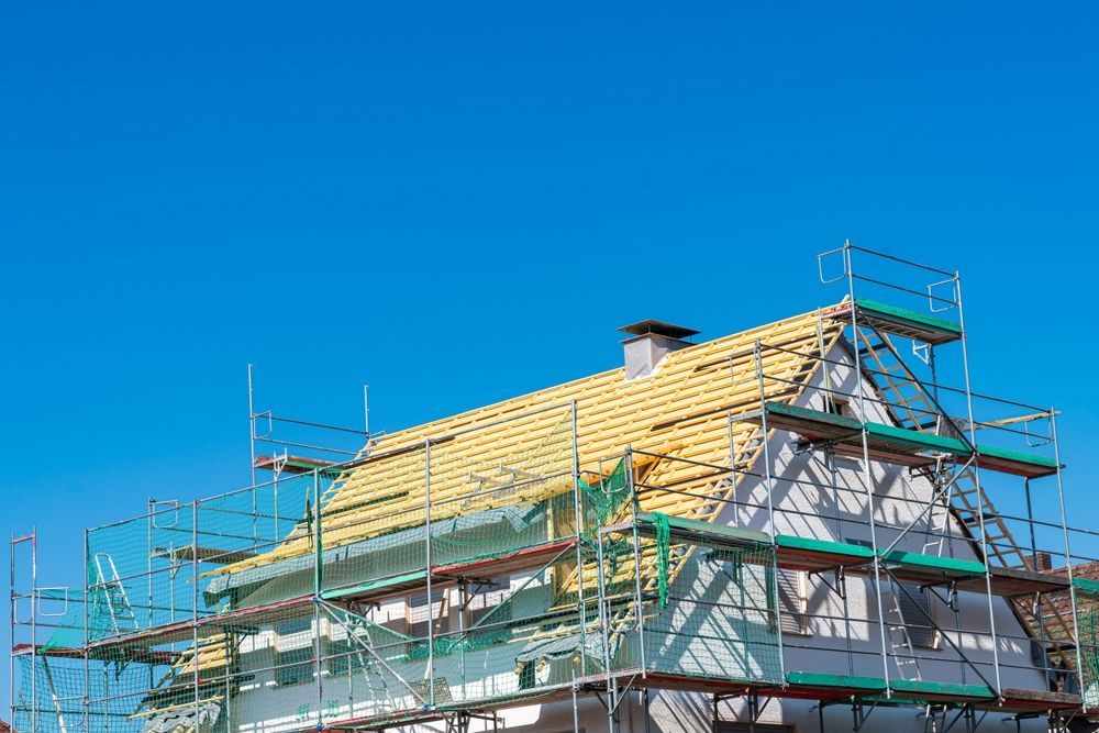 Scaffolding around a house with a yellow roof under a clear blue sky