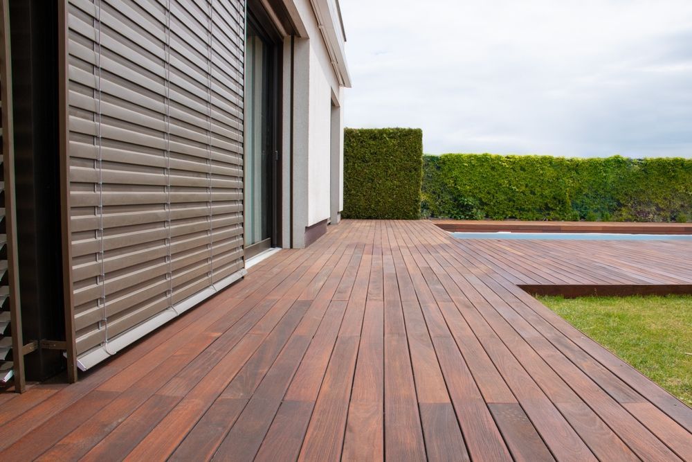 Modern patio with wooden deck, hedge privacy screen, and a pool beside a house exterior