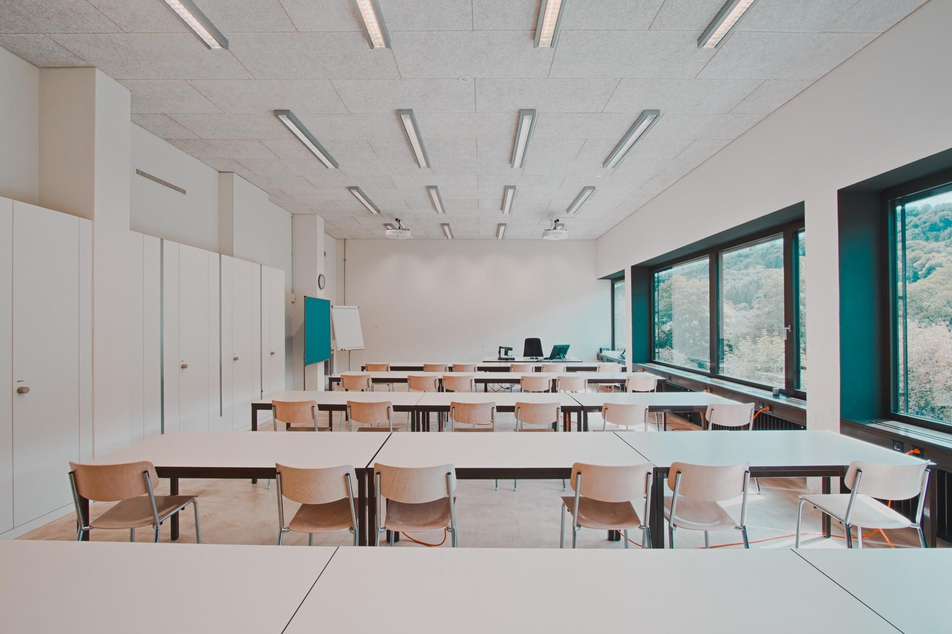 Ein leeres Klassenzimmer mit Tischen und Stühlen und vielen Fenstern.