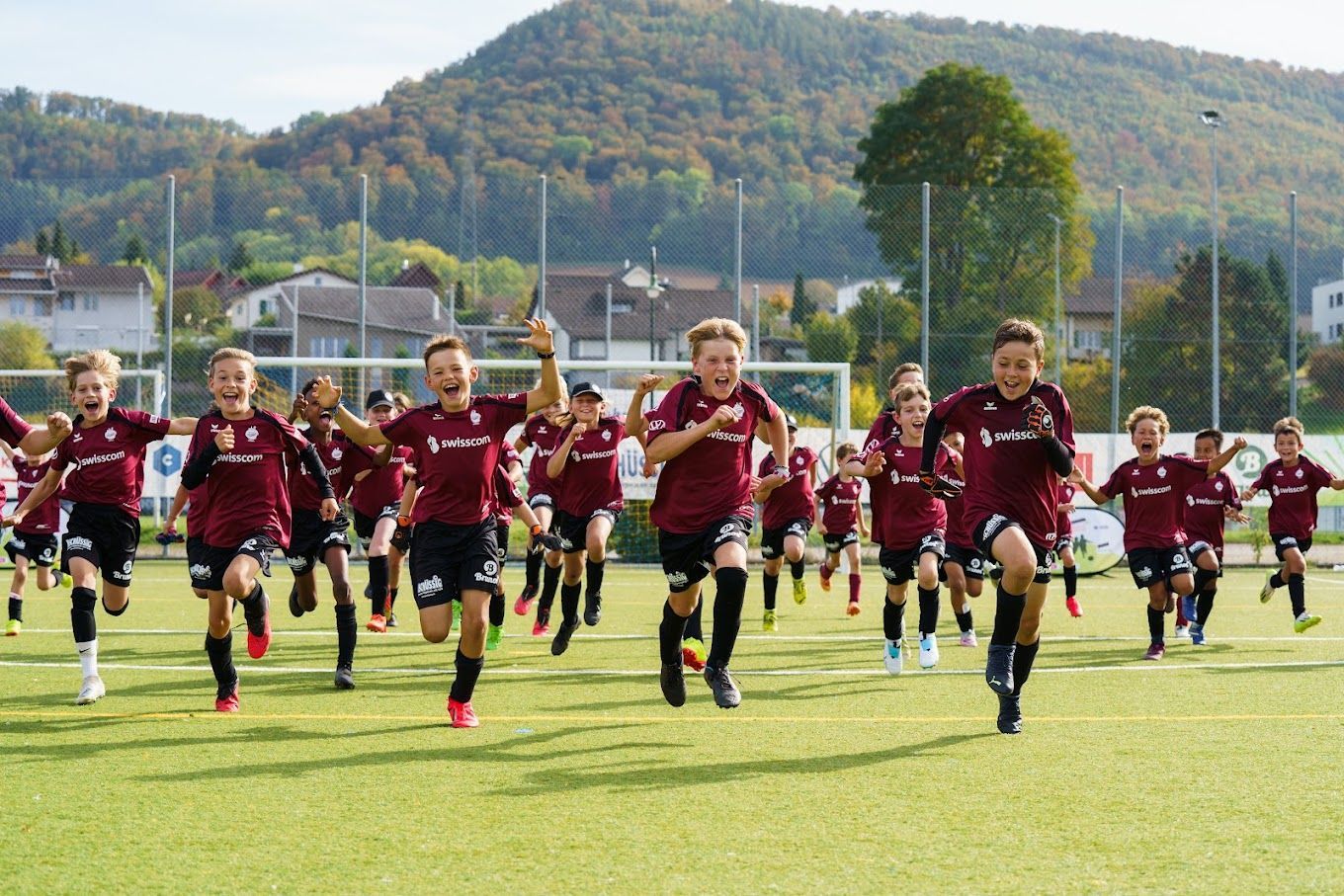 Kinder in einem roten Fussballtrikot rennen auf einem Fussballplatz herum