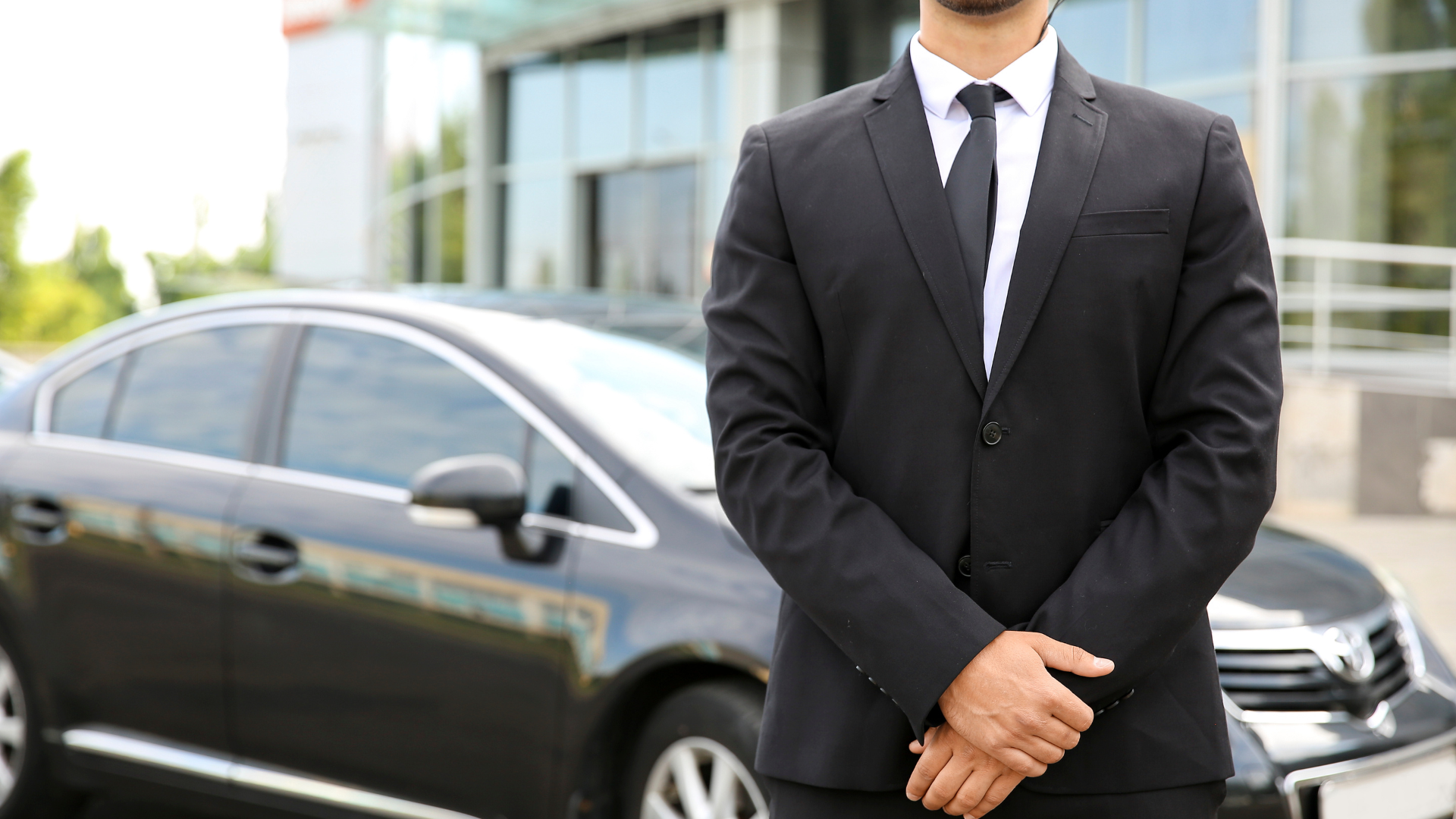 A man in a suit and tie is standing in front of a car.