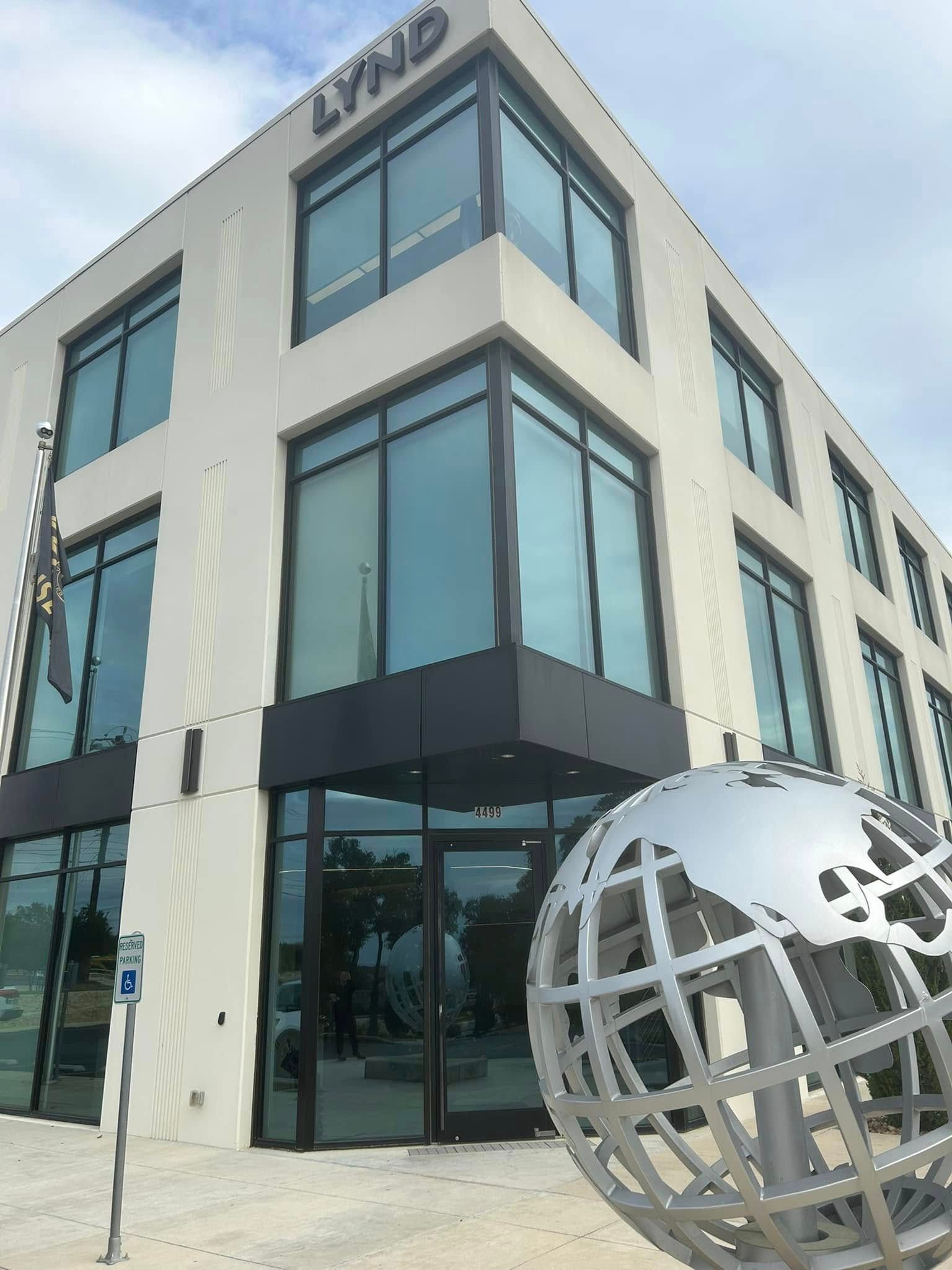 A modern three-story building with the word LYND on top, featuring glass windows and a metal globe sculpture in front.
