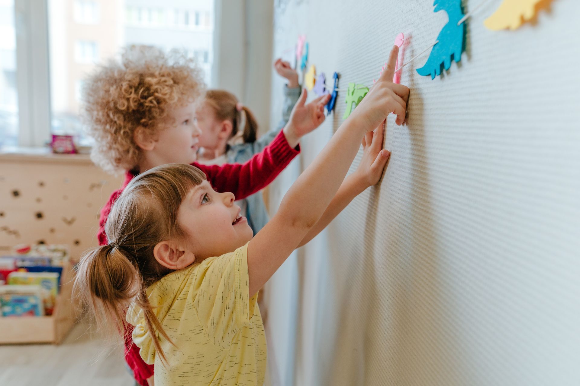 Children placing shapes on a classroom learning wall.