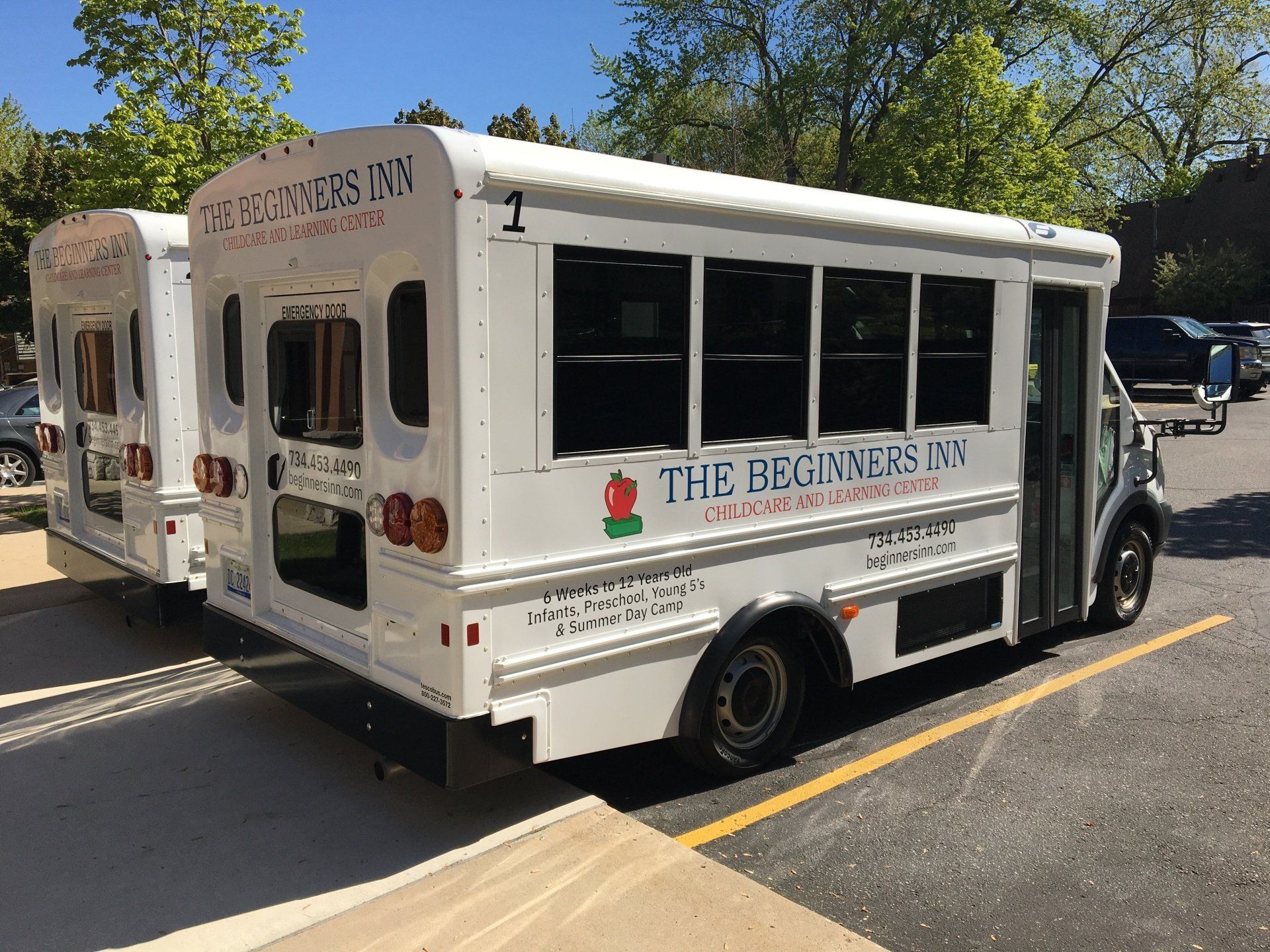 Two white buses parked in front of a building. Each bus has the name 