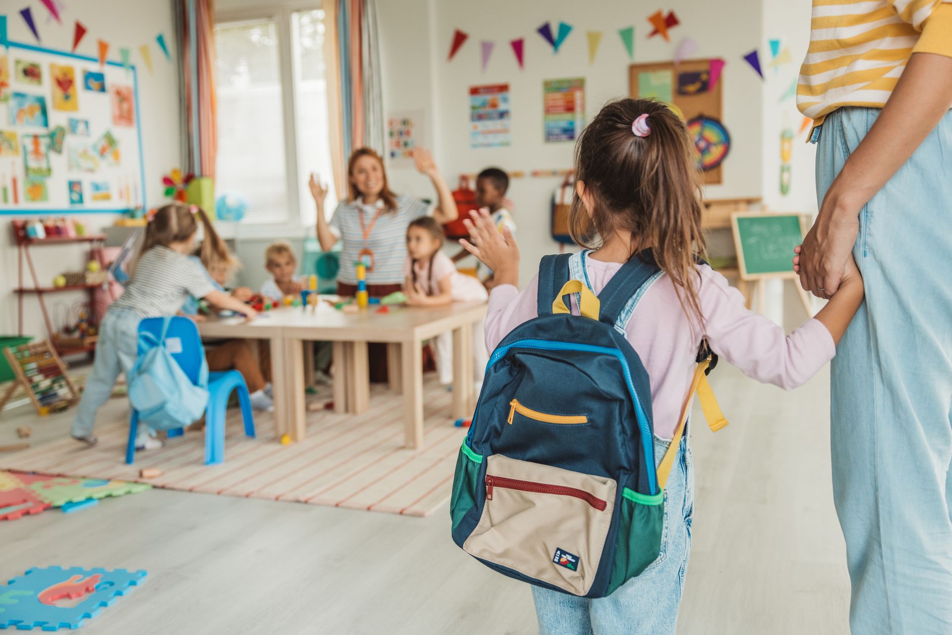 Preschool teacher in kindergarten classroom greeting new student.