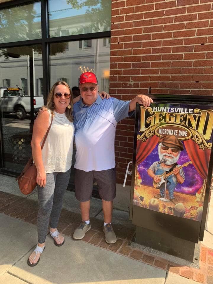 A man and a woman are posing for a picture in front of a brick building.