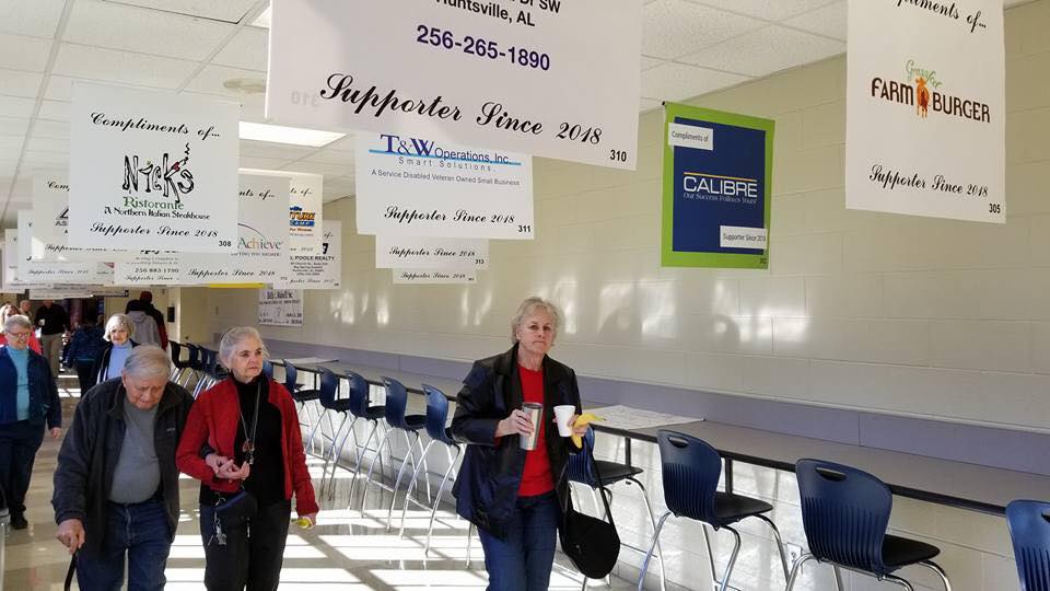 A group of people are walking down a hallway with signs hanging from the ceiling.