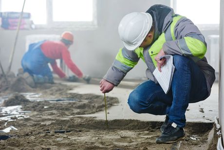 A construction worker is measuring the floor with a tape measure.