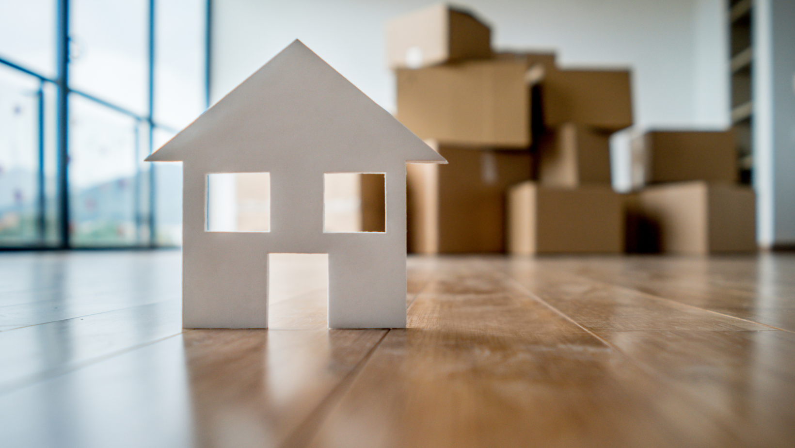 A model house is sitting on a wooden floor in front of a pile of cardboard boxes.