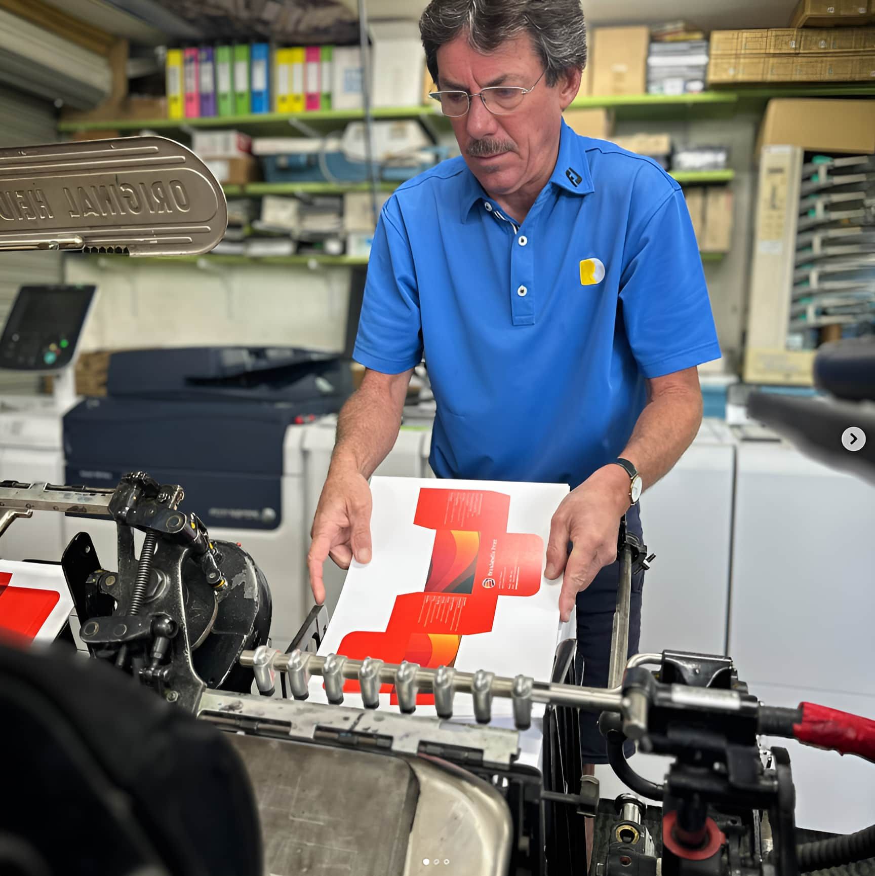 A Man in a Blue Shirt is Holding a Piece of Paper With a Red Cross on It — Brindabella Print In Pearce, ACT