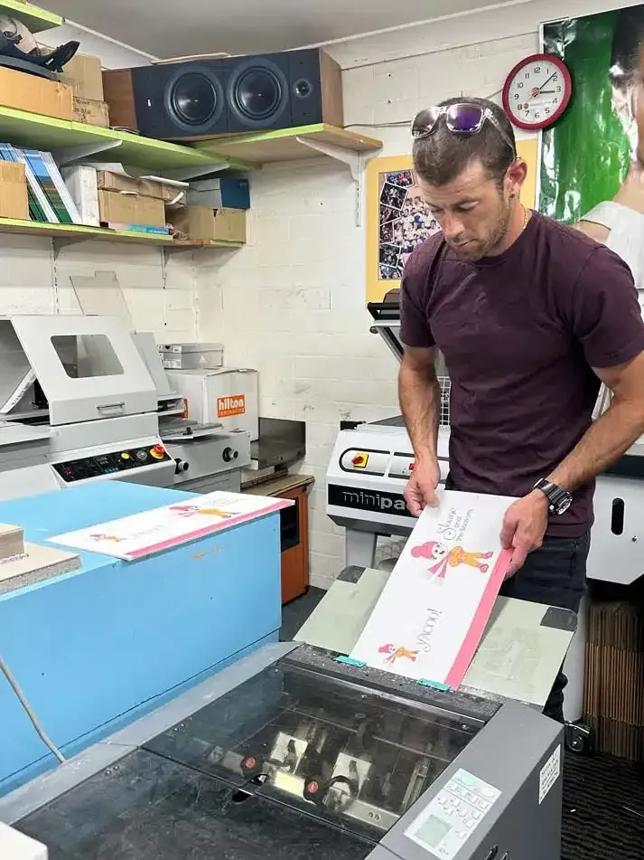 A Man is Standing in Front of a Machine Holding a Piece of Paper — Brindabella Print In Pearce, ACT