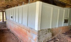 a brick wall with white siding is under a wooden deck.