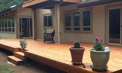 a large wooden deck with potted plants on it in front of a house.