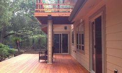 a large wooden deck with a bench and sliding glass doors on the side of a house .