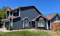 a large house with a blue siding and a brown roof is sitting on top of a lush green lawn .