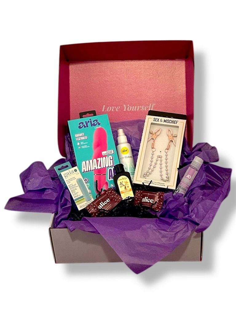 A box with adult pleasure products, including a vibrator, nipple clamps, and other items, on purple tissue paper.