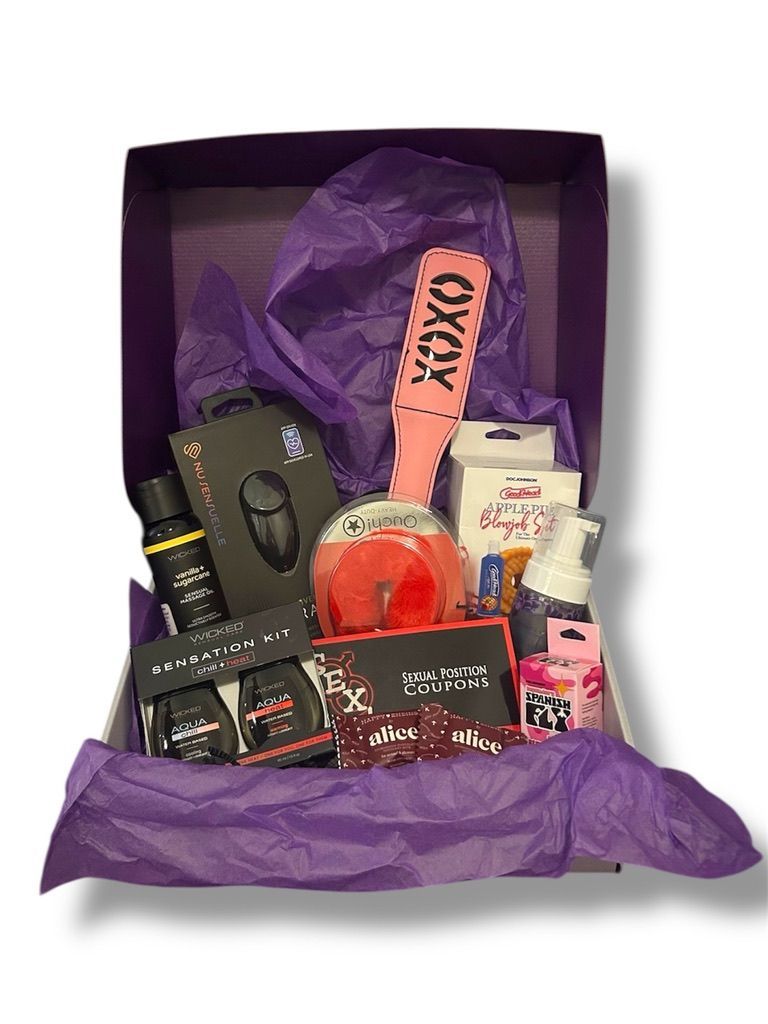 Purple gift box filled with various sex toys and lubricants, all against purple tissue paper.