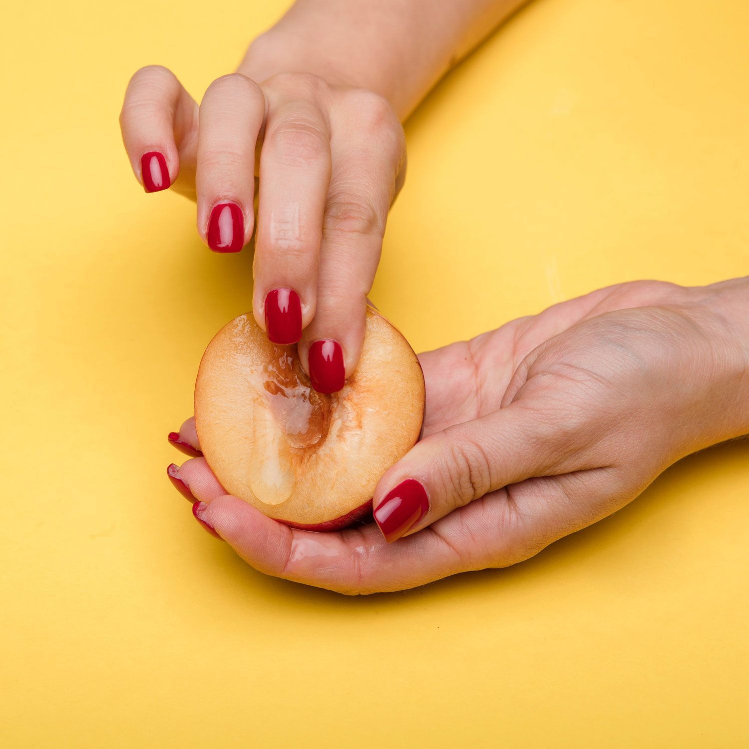 A woman 's hands with red nails are holding a slice of apple.