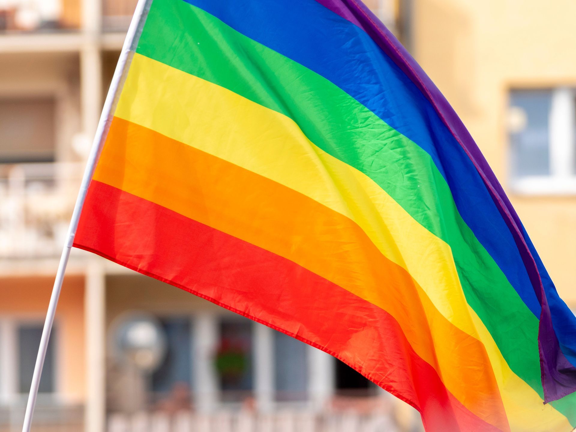 Rainbow pride flag waving outdoors against a blurred building background