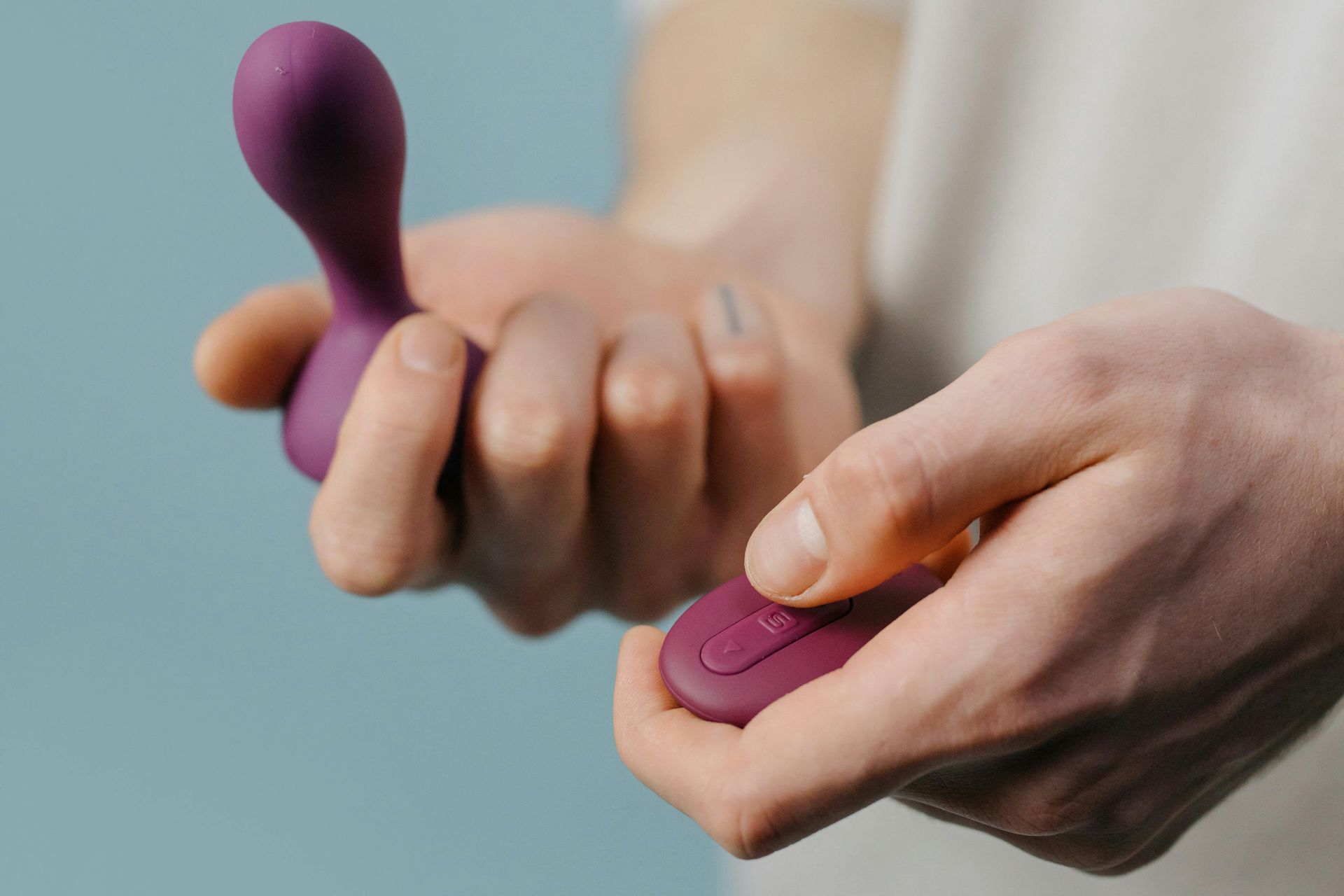 Hands holding purple and pink sex toys against a blurred background