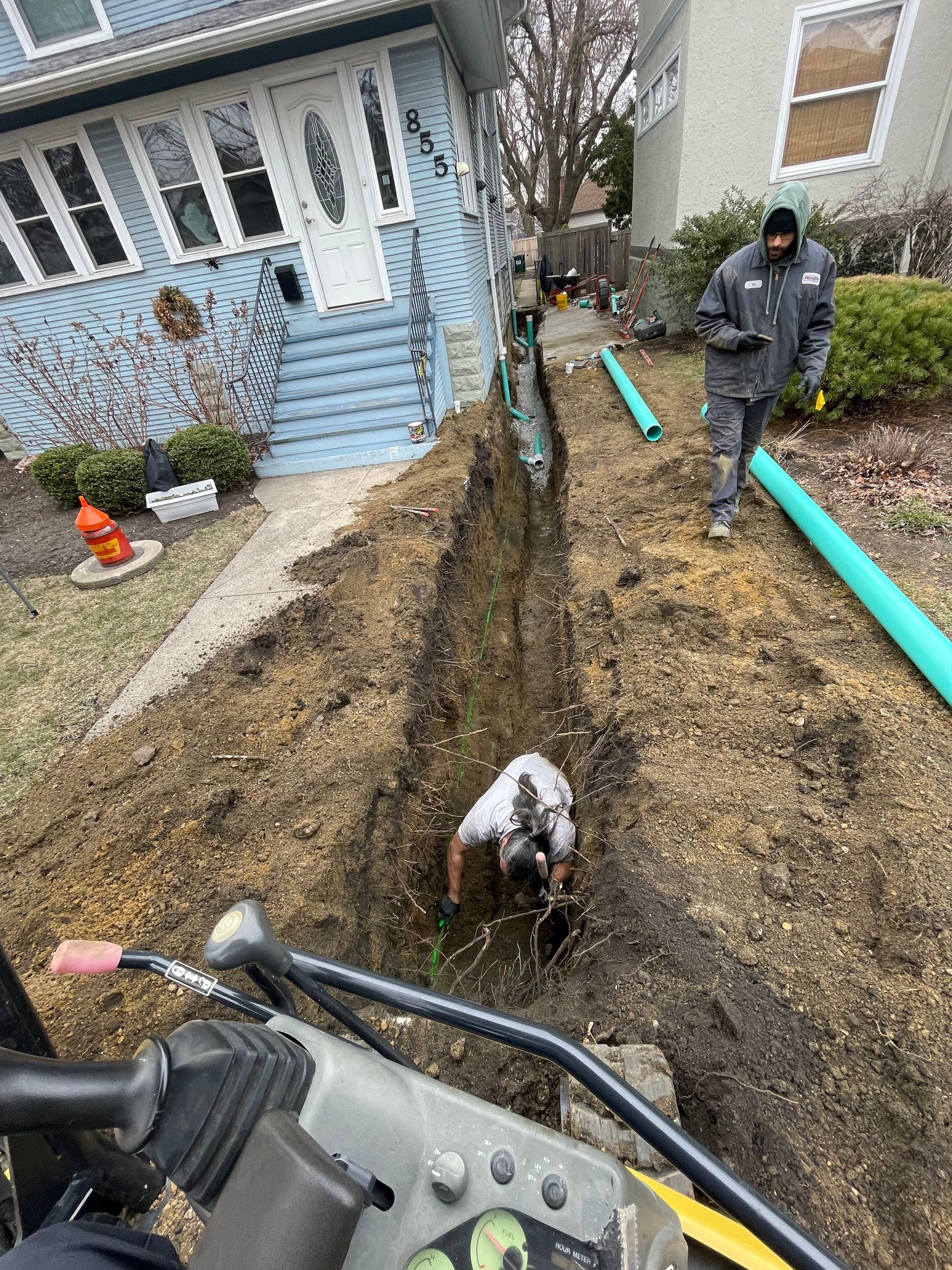 Plumber installing residential sewer line with trench excavation near home in Chicagoland
