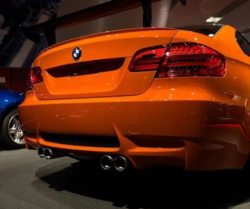 Orange BMW sports car with quad exhaust pipes and rear spoiler.