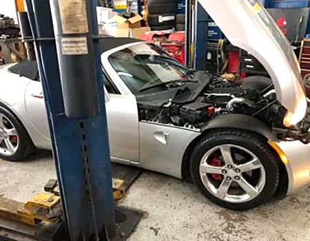 Silver convertible car with hood open in a repair shop.