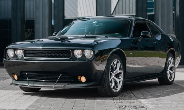 Black Dodge Challenger parked in front of a modern building with a glass facade. The car has a sporty design.