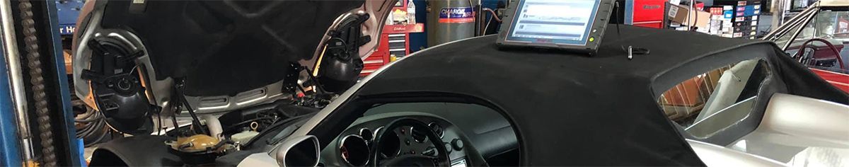 A black motorcycle's dashboard and windshield are in focus, with chrome elements visible in a cluttered workshop setting.