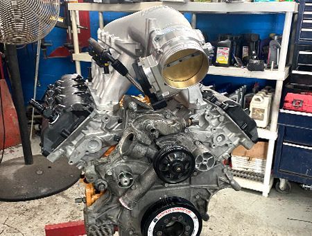 An engine with a silver intake manifold and throttle body is in a garage setting.