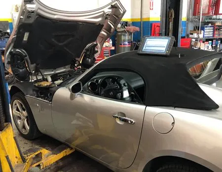 Silver convertible in auto repair shop with hood open and laptop on the dashboard