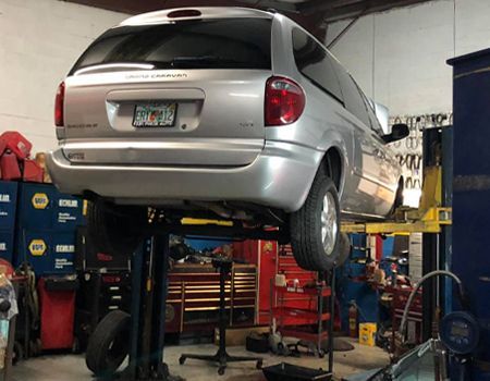 Silver minivan lifted on a hydraulic hoist in an auto repair shop, showing its underside for maintenance.