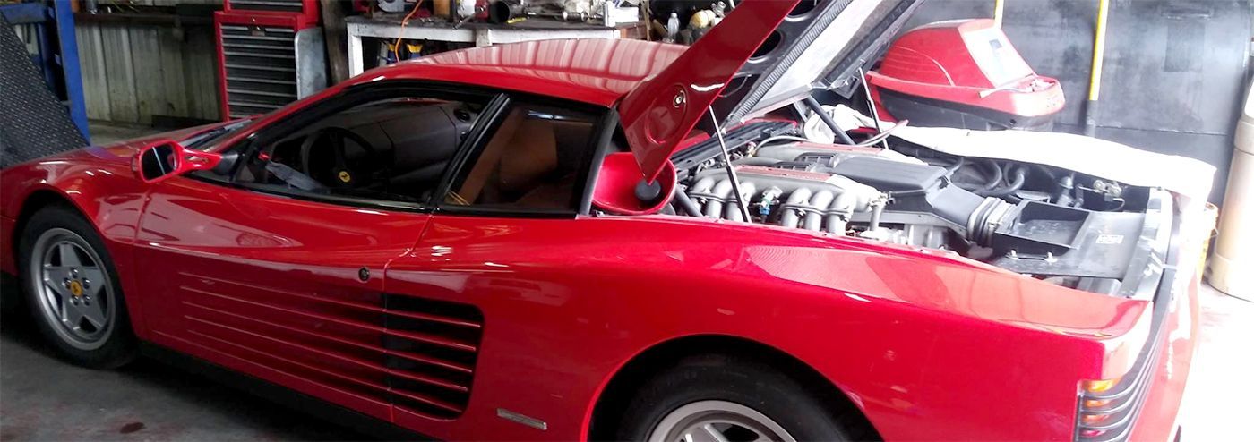 A red Ferrari Testarossa with the hood open, likely in a garage.