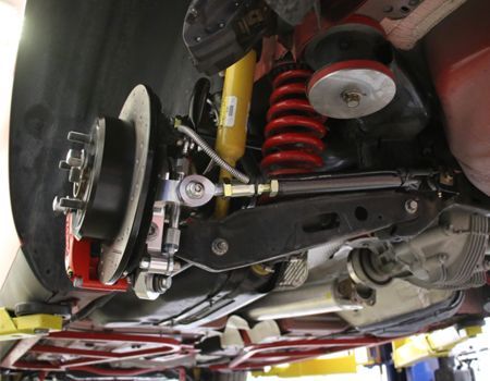 Undercarriage of a red car showing rear suspension and brake components. Includes a coilover shock, brake rotor, and control arms.