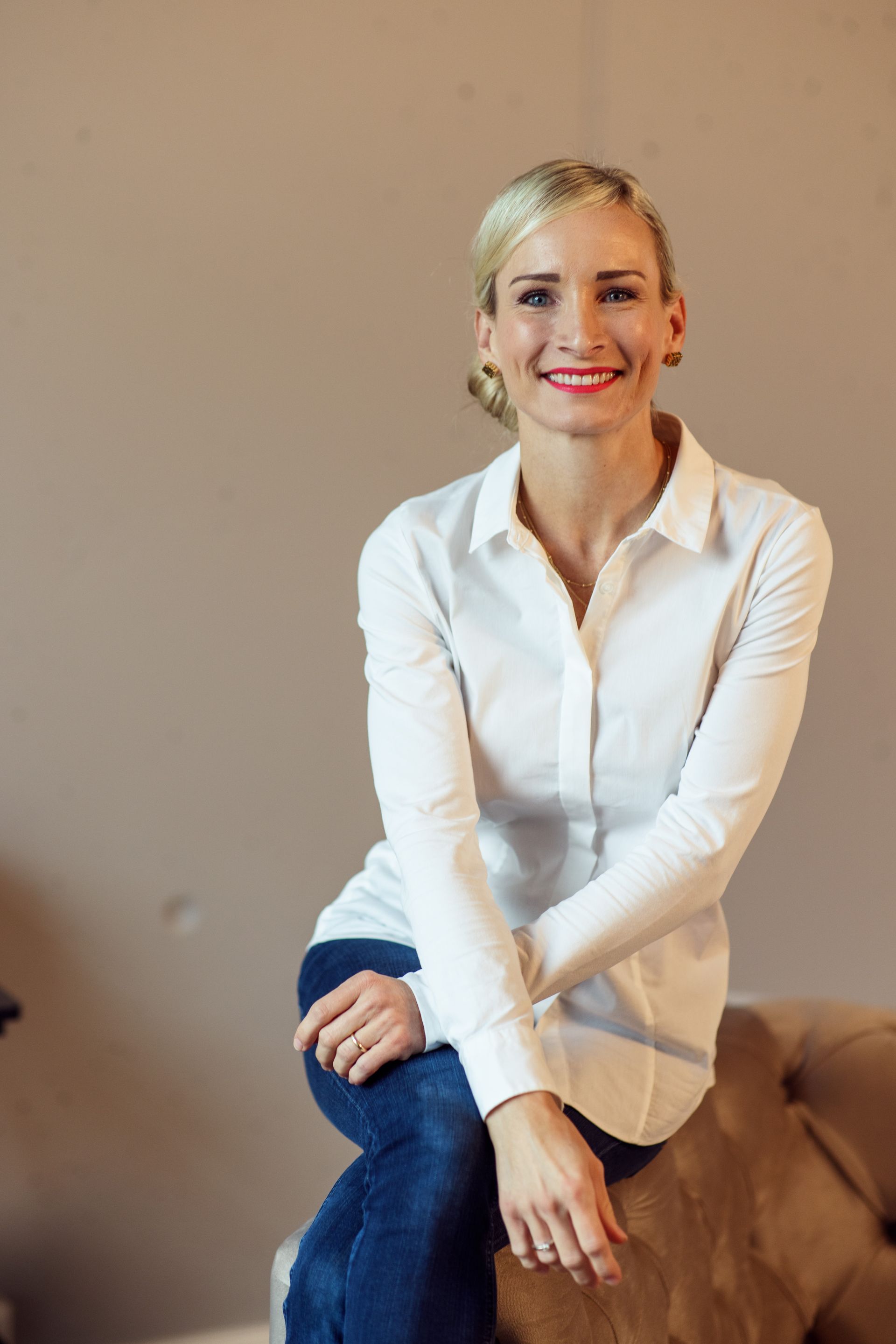 Eine Frau in einem weißen Hemd und Jeans sitzt auf einem Sofa.