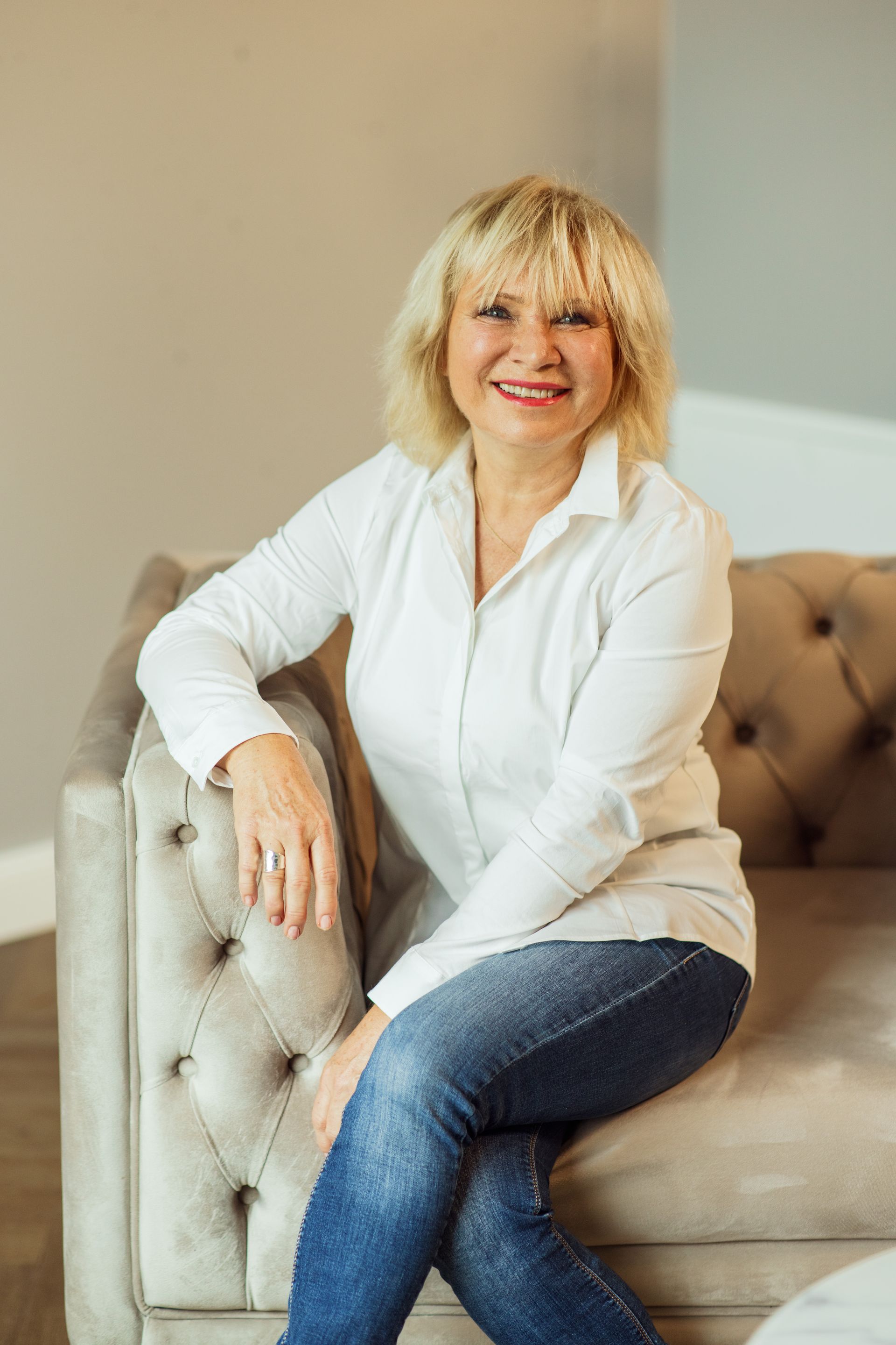 Eine Frau sitzt mit überkreuzten Beinen auf einem Sofa und lächelt.