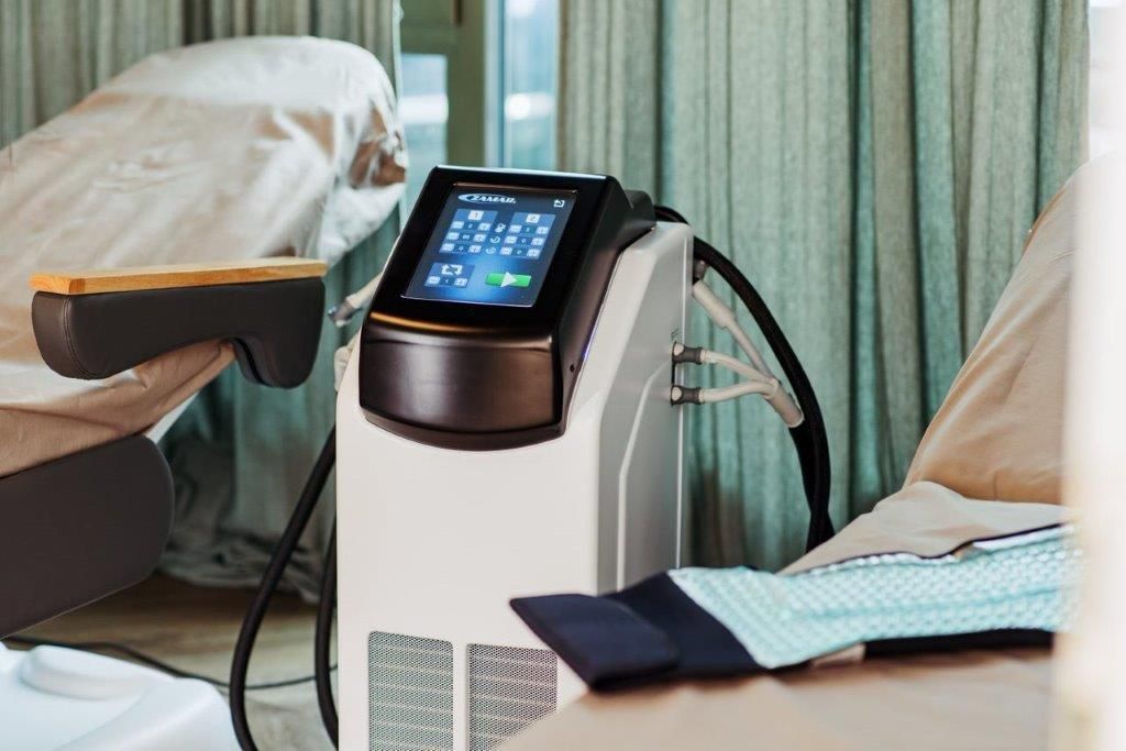 In einem Krankenhauszimmer steht eine Maschine auf einem Tisch neben einem Bett.