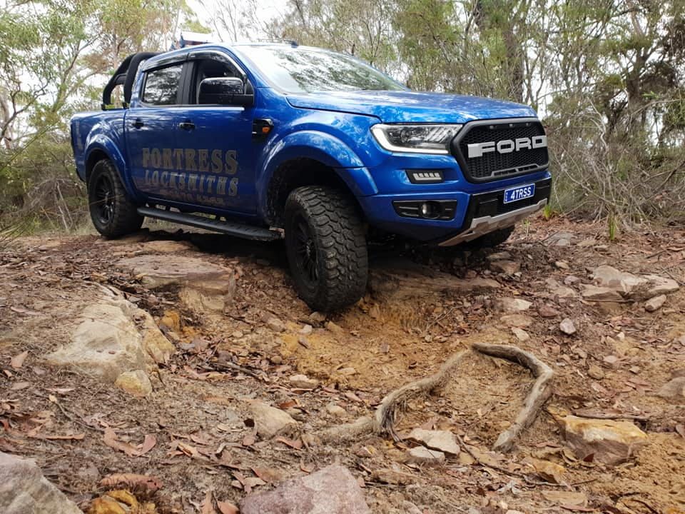 A Blue Ford Ranger Raptor Is Driving Down A Dirt Road — Fortress Locksmiths & Security in Hornsby, NSW