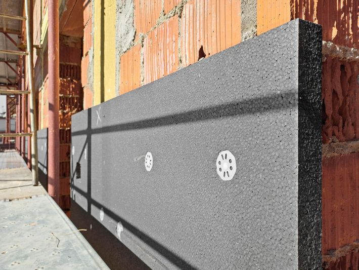 Pannelli isolanti grigi fissati a un muro di mattoni con tasselli circolari bianchi durante un progetto di costruzione.