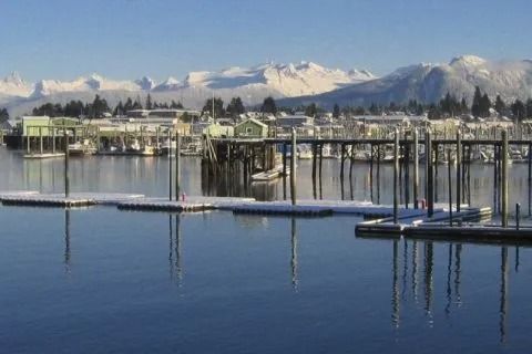 Snowy mountains beyond a calm marina with docks and boat slips under a clear blue sky