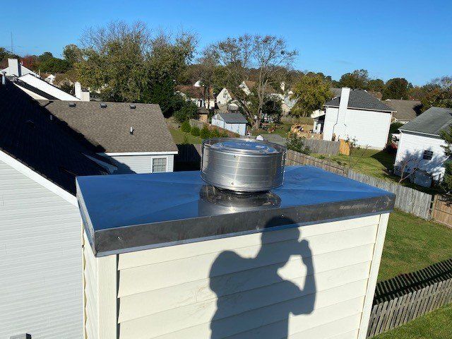 A shiny metal chimney cap with a rotating cowl on a house roof, a shadow of a person is visible on the front.