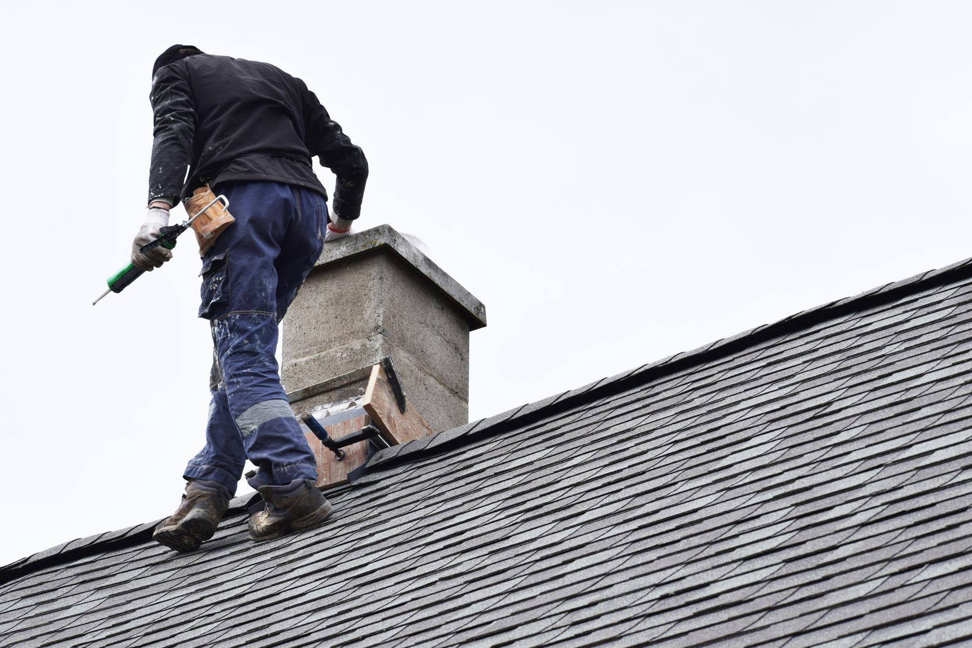 A worker fixing a chimney atop a grey slate roof of a residential house.