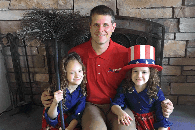 Man and two young girls, celebrating a patriotic event. Man wears a red shirt, girls are in blue outfits.
